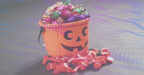 Jack-o-lantern bucket overflowing with wrapped chocolates and gummy candies for halloween