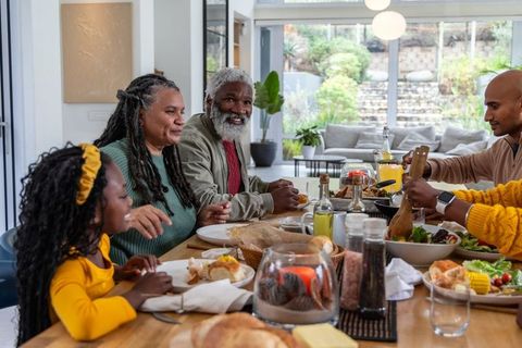 Multigenerational african american family sharing dinner at sunlit open-plan dining table