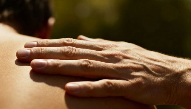 Adult hand resting on bare shoulder in sunlight highlighting veins and fingernails