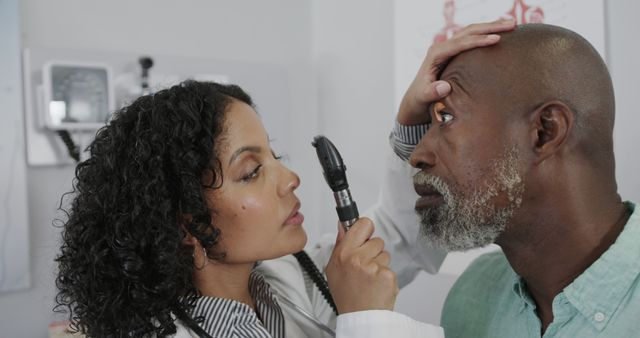 Female doctor using an ophthalmoscope while performing an eye checkup on a senior male patient in a clinical setting. Suitable for use in healthcare, medical services, hospital information, elderly care, and ophthalmology-related content.