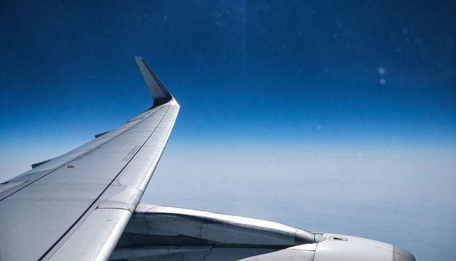 Wingtip window view over cloud deck at cruising altitude with jet engine and deep blue sky