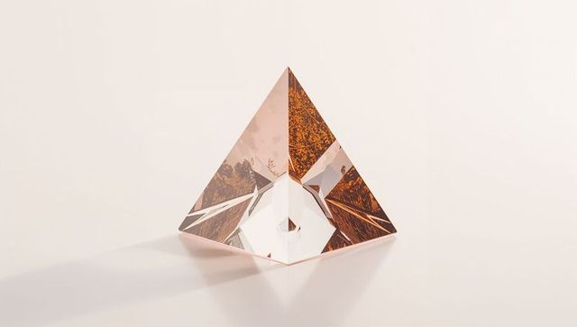 Faceted glass pyramid prism refracting warm amber light on pale cream surface with shadow