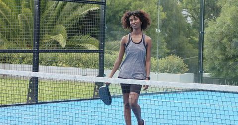 Woman walking on blue paddle court holding paddle wearing casual athletic outfit