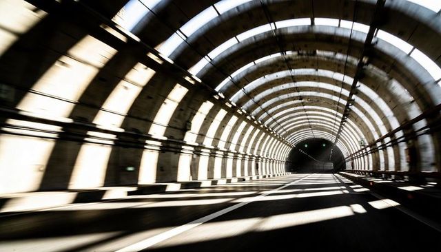Sunlit concrete arched tunnel stretching into distance with dramatic shadow stripes