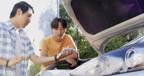 Father and Teenage Son Repairing Car in Driveway