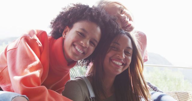 Perfect for highlighting themes of friendship and diversity, this photo captures three young adults with different ethnic backgrounds smiling and enjoying each other's company outdoors. It is great for use in marketing materials that aim to promote teamwork, social events, casual gatherings, or discussions on diversity and inclusion.