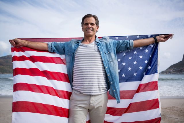 Man standing on beach holding American flag, expressing patriotism and pride. Suitable for themes related to national holidays, patriotism, travel, and outdoor activities.