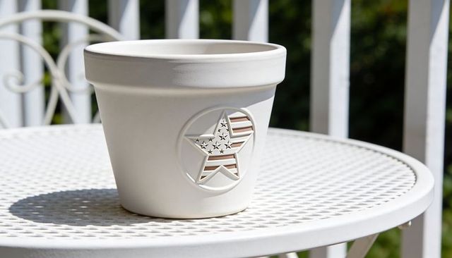 Sunlit white ceramic planter with embossed american star sitting on round metal patio table