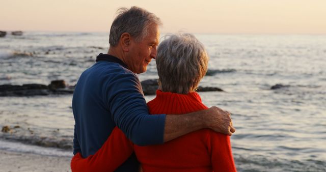 This image of an elderly couple embracing on a beach at sunset conveys emotions of love, togetherness, and relaxation. Ideal for use in marketing materials for retirement communities, travel agencies promoting senior vacations, or articles on love and relationships in old age.