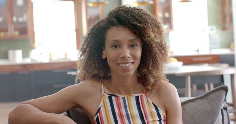 Smiling Biracial Woman in Colorful Striped Top Relaxing Indoors