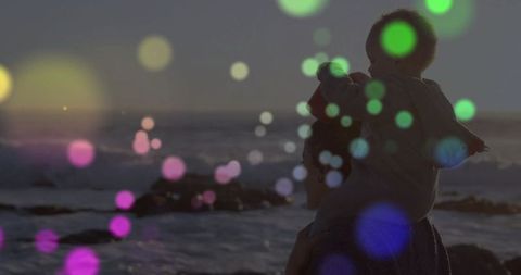 Mother holding baby at sunset with dreamy bokeh effect on coast
