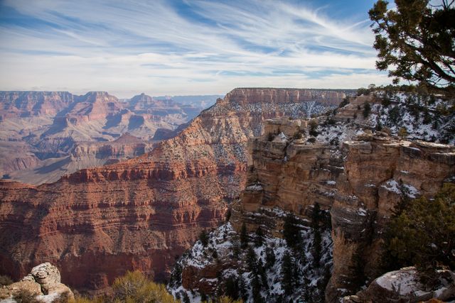 Beautiful winter landscape of the Grand Canyon with snow-covered cliffs under a cloudy sky. The mix of snow and red rock formations creates a stunning contrast in this iconic national park. Ideal for travel brochures, nature documentaries, or as inspirational nature backgrounds.