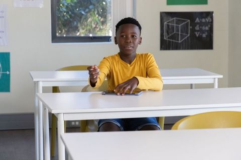 African american student raising hand while using tablet in bright classroom featuring yellow chairs