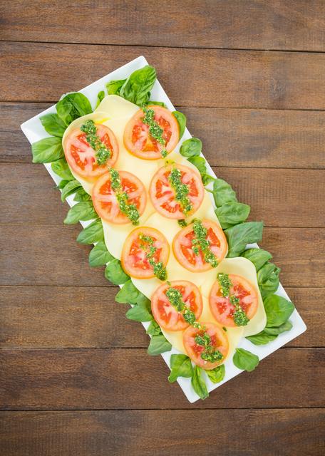 Caprese salad with sliced tomatoes, mozzarella cheese, and basil leaves arranged on a rectangular white tray placed on a wooden board. Ideal for use in food blogs, restaurant menus, healthy eating promotions, and culinary magazines.