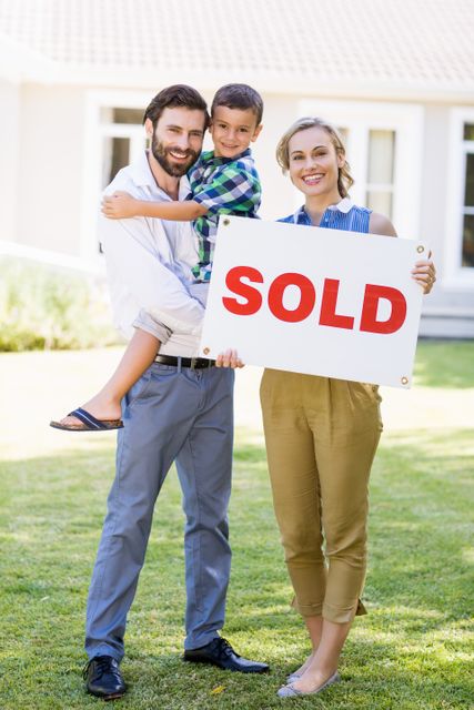 Portrait of happy family standing outside home with sold sign