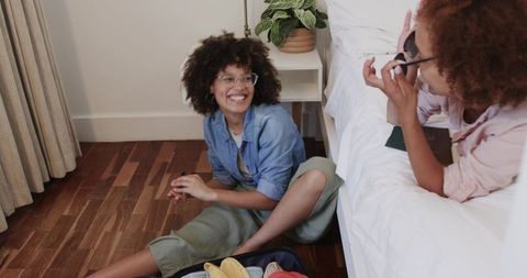 African American friends packing suitcase and laughing on bedroom floor, casual travel