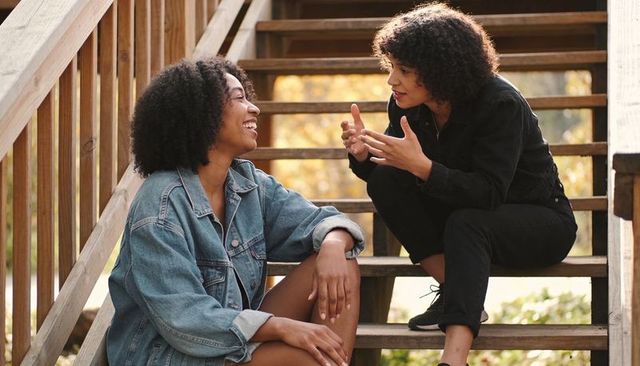 Friends chatting and laughing on wooden outdoor stairs during golden autumn sunlight