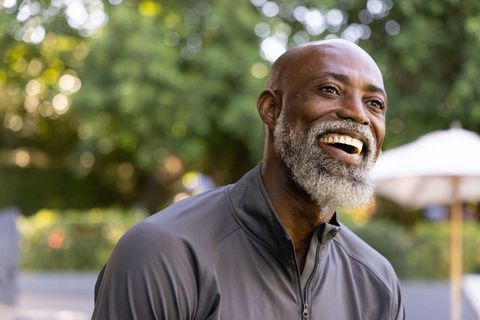 Laughing senior african man looking up outdoors with white beard and zipped jacket