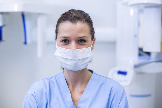 Dental assistant wearing surgical mask in a dental clinic. Ideal for use in healthcare, dental care, and medical industry materials. Can be used in brochures, websites, and advertisements promoting dental services, hygiene practices, and healthcare professionalism.