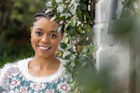 African american woman smiling in fuzzy knit sweater with cornrows near ivy-covered wall