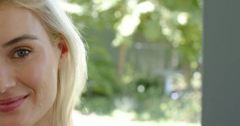 Smiling blonde woman leaning in doorway with sunlit garden bokeh and ample copy space