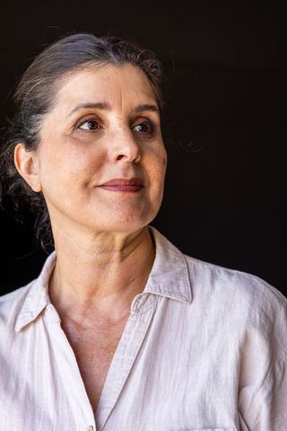 Contemplative mature woman looking right wearing linen shirt studio portrait dark backdrop