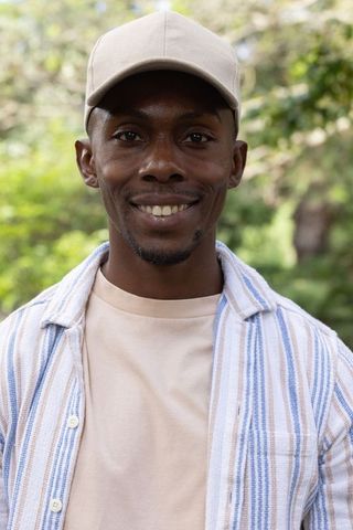 African american man smiling and looking at camera outdoors wearing beige cap, striped shirt