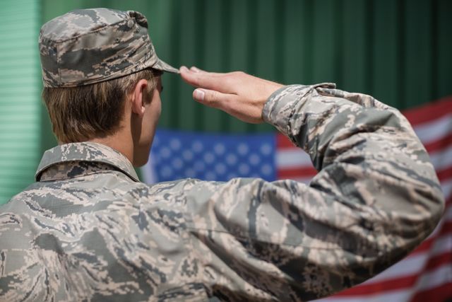 This image depicts a military soldier in uniform saluting the American flag at a boot camp. It can be used to illustrate themes of patriotism, military service, respect, and national pride. Suitable for use in articles, advertisements, and educational materials related to the armed forces, national holidays, and veteran affairs.