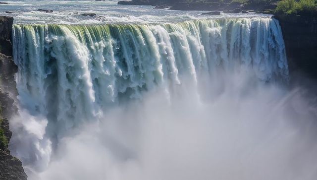 Cascading waterfall curtain pouring over cliff with towering mist plume in river gorge