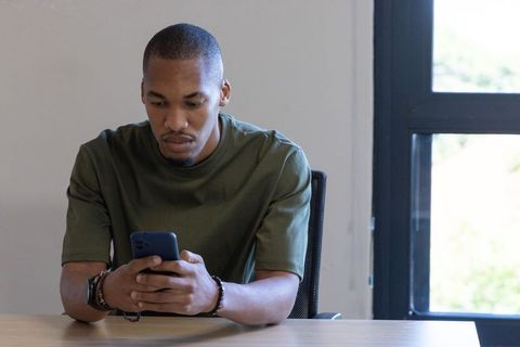 Focused african american man using smartphone at modern minimalist workspace, daylight
