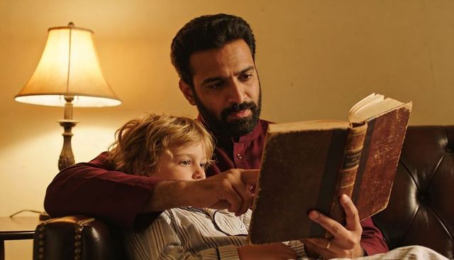 Father reading bedtime story to child on sofa under warm lamp light, cozy family moment