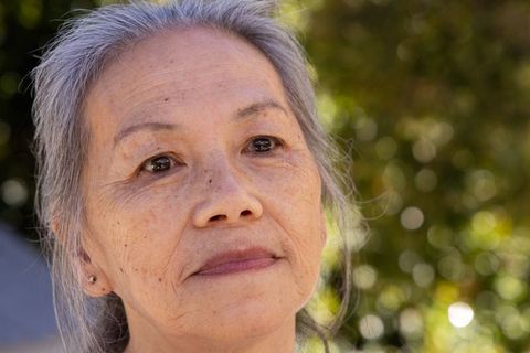 Senior asian woman gazing upward with serene expression in sunlit garden portrait