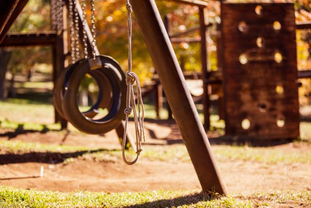 Rope hanging by tire swings in a sunny park with autumn foliage in the background. Ideal for illustrating concepts of childhood, outdoor activities, and recreational spaces. Suitable for use in articles about playground safety, outdoor play, and family-friendly parks.