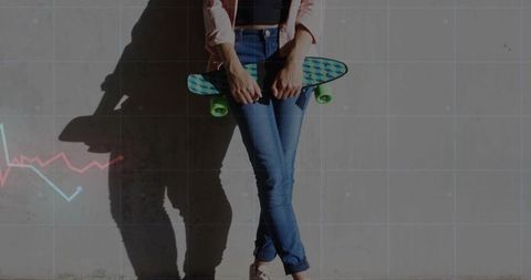 Young woman leaning against concrete wall holding teal skateboard casting long shadow