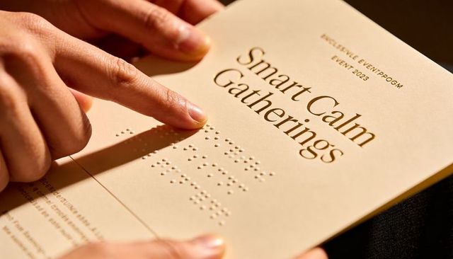 Tracing Fingertip Along Braille on Embossed Smart Calm Gatherings Booklet in Warm Light