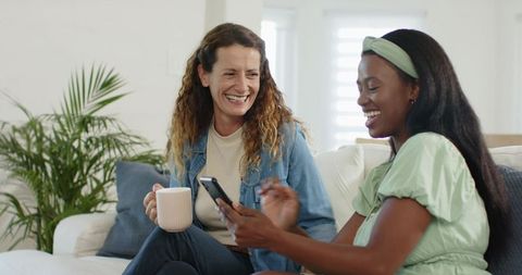 Happy Friends Chatting on Sofa with Coffee and Smartphone