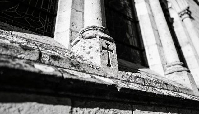 Highlighting carved stone cross casting shadow on weathered gothic church facade ledge