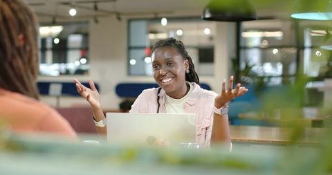 African American woman smiling and gesturing while working on laptop in modern coworking space