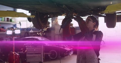 Female mechanic grinding car underside with sparks in garage workshop