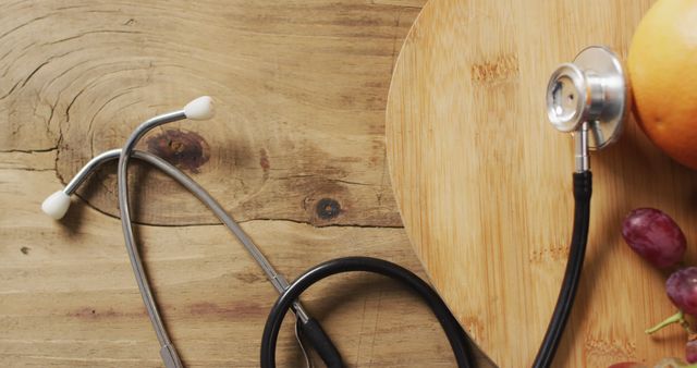 Stethoscope lying next to an orange and grapes on a rustic wooden surface. Image conceptually links health, nutrition, and medicine. Useful for articles, blogs, or materials promoting healthy living, medical advice, or diet.