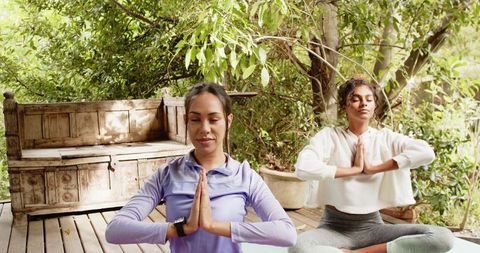 Diverse women meditating on deck in natural setting