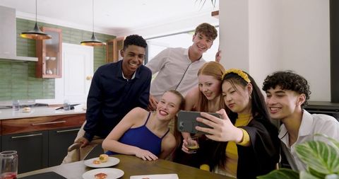 Group taking selfie in modern kitchen during casual friends gathering with appetizers