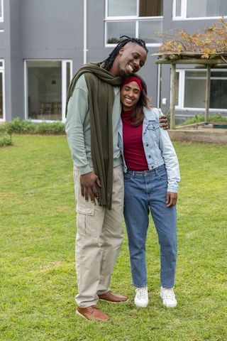 Multicultural couple embracing on lawn by modern building smiling in casual denim