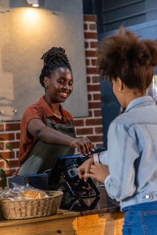 Smiling african american barista accepting contactless smartwatch payment at cafe counter