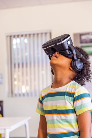 African american boy exploring virtual reality with headset and headphones in classroom