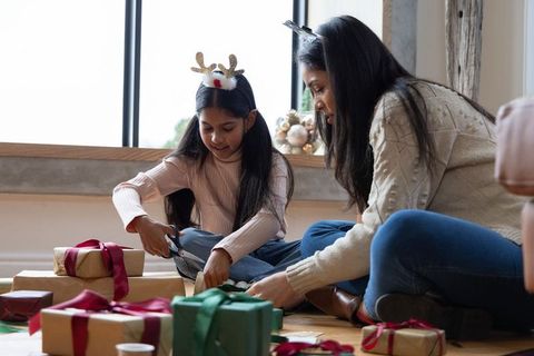 Indian mother and daughter wrapping christmas gifts at home, cozy family crafting with ribbons