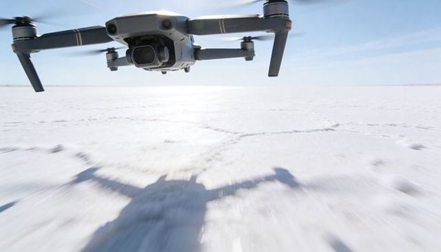 Hovering Camera Drone Over Frozen Salt Flat Casting Dramatic Shadow and Motion Blur