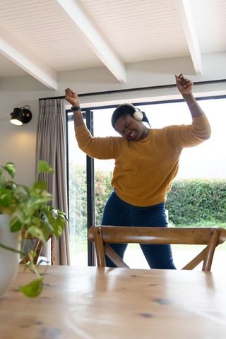 African american woman dancing with headphones by sliding glass doors in dining room
