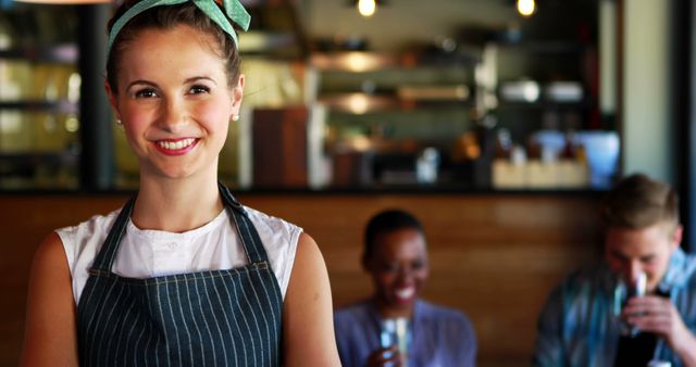 Smiling Cafe Worker in Apron with Happy Customers in Background - Download Free Stock Images Pikwizard.com