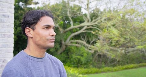 Contemplative man standing and gazing outdoors near pale brick wall with garden backdrop